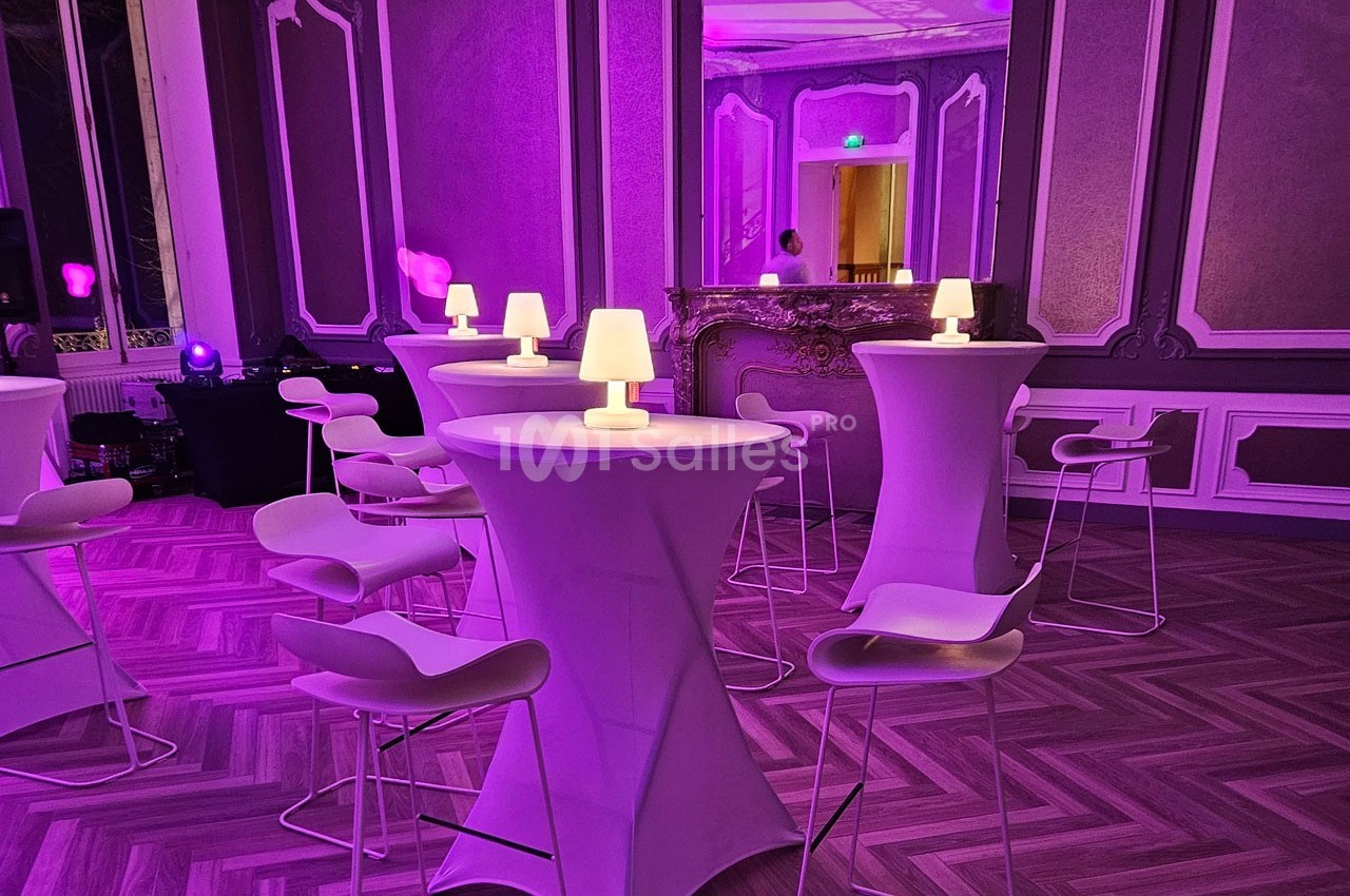 Salle élégante avec tables hautes, chaises design et éclairage violet créant une ambiance tamisée.