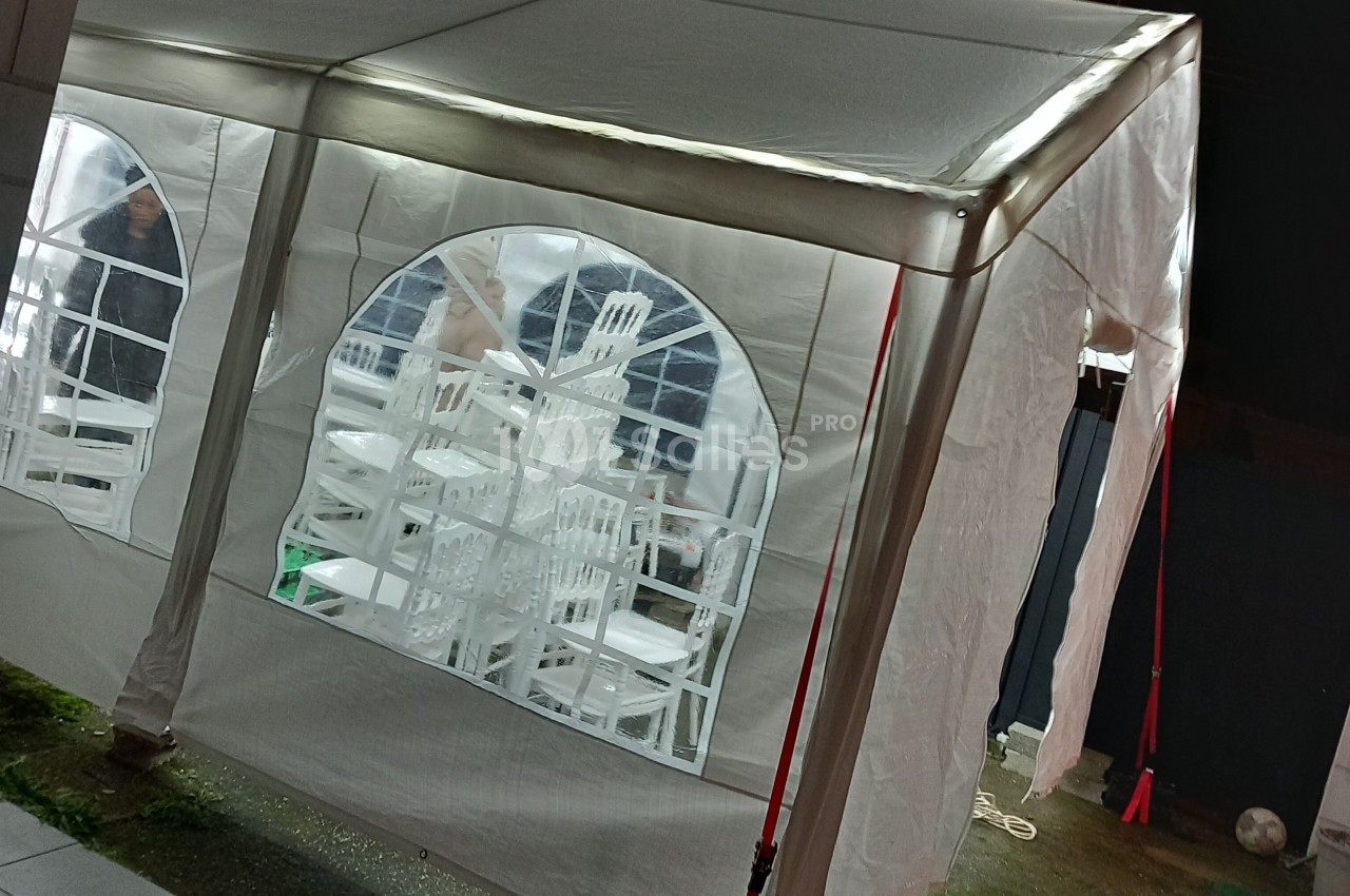 Tente blanche éclairée avec des chaises empilées visibles à travers les fenêtres en plastique transparent.