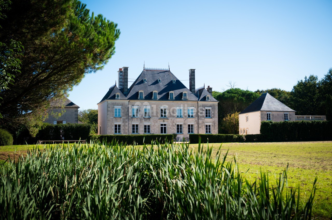 Manoir en pierre entouré de verdure, avec pelouse au premier plan et ciel dégagé en arrière-plan.