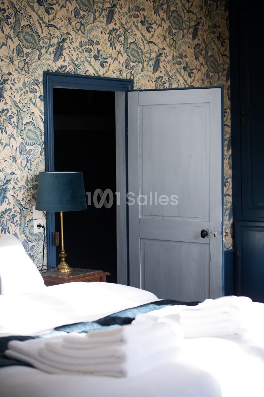 Chambre avec lit, lampe sur table de chevet, mur tapissé à motifs floraux et porte entrouverte.