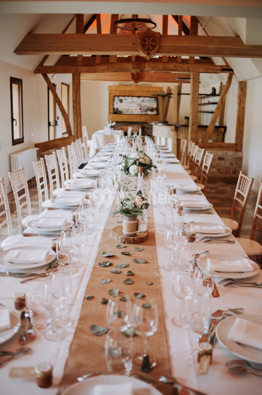 Grande table de réception décorée avec nappes blanches, chemins de table en toile de jute, fleurs et vaisselle élégante.