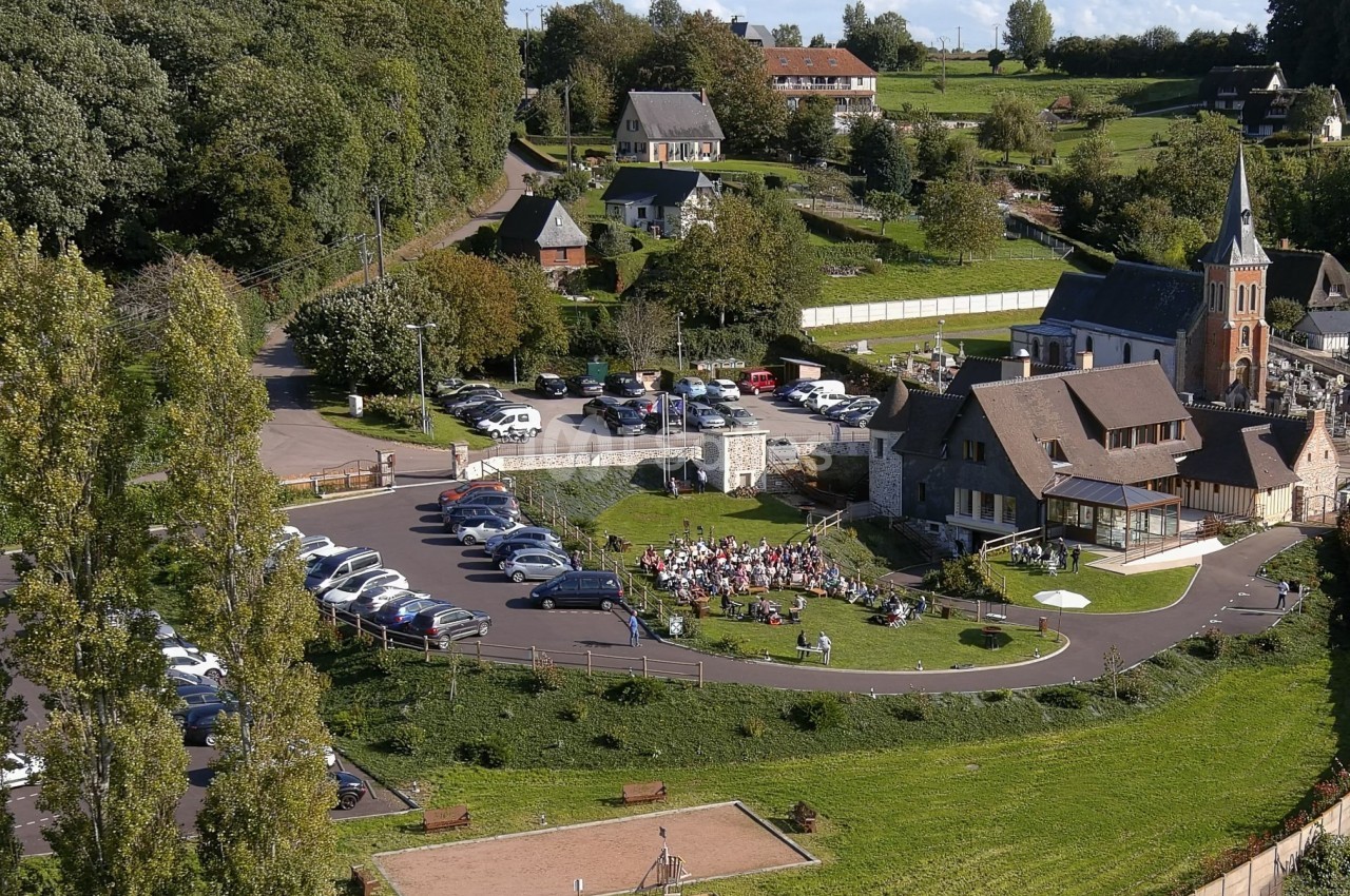 Vue aérienne d'un village avec une église, un parking, une aire de jeux et un rassemblement en plein air.