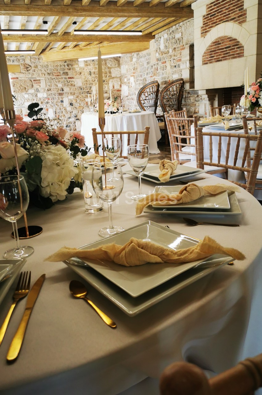 Table dressée avec élégance dans une salle en pierre, ornée de fleurs, bougies et vaisselle raffinée.
