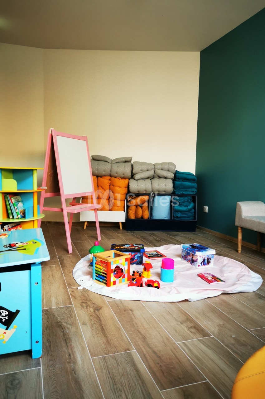 Salle de jeux pour enfants avec tapis, jouets, tableau blanc et étagères colorées sur un sol en bois.