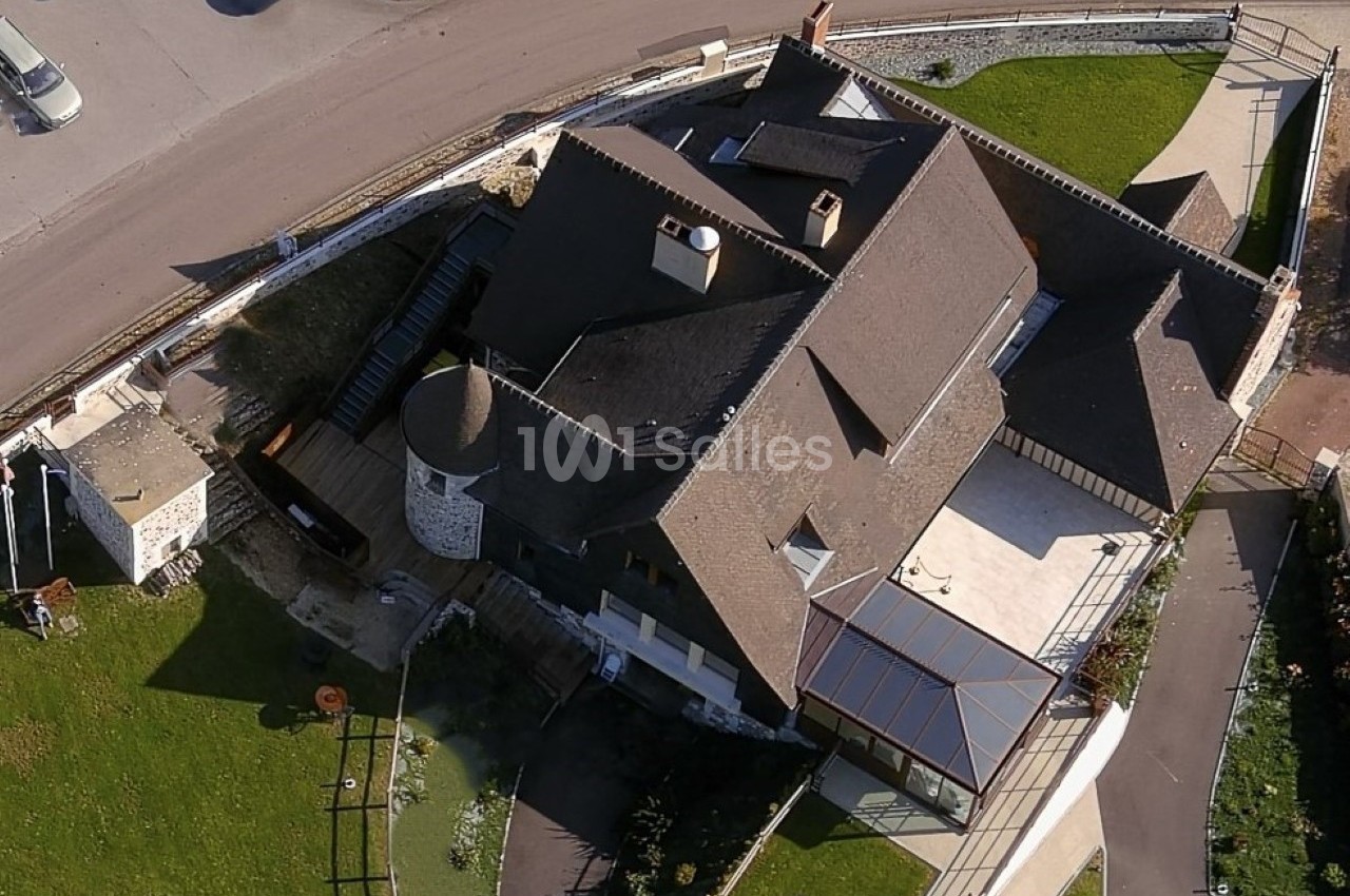 Vue aérienne d'un bâtiment avec toit en pente, terrasse, véranda et espaces verts environnants.