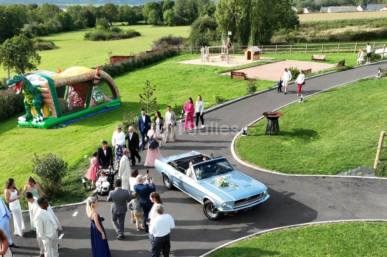 Un groupe de personnes rassemblé autour d'une voiture décapotable bleue dans un parc avec une aire de jeux en arrière-plan.
