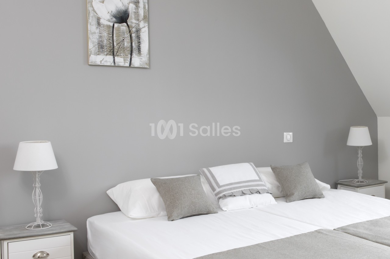Lit double avec linge de lit gris et blanc, encadré par deux tables de chevet assorties avec lampes, dans une chambre…