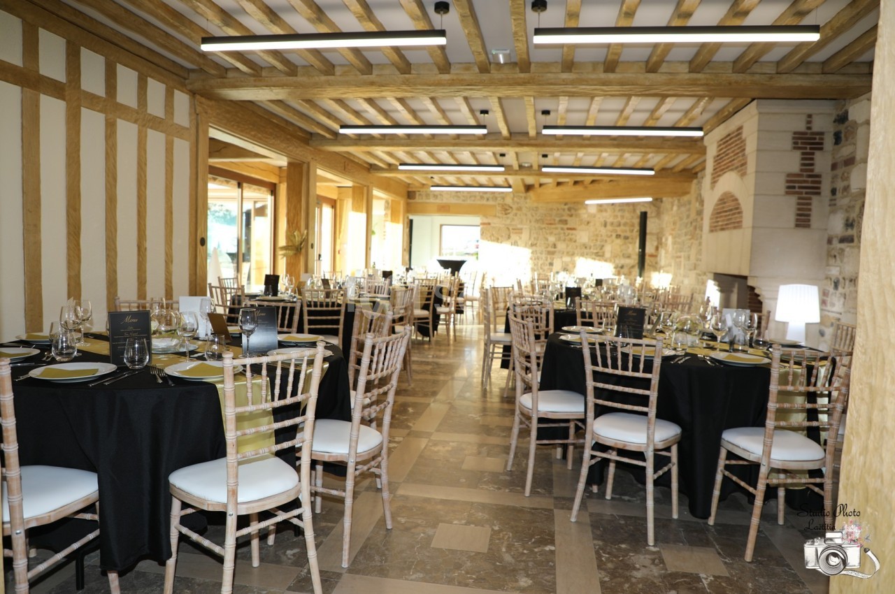 Salle de réception lumineuse avec tables dressées, chaises en bois clair et murs en pierres apparentes.