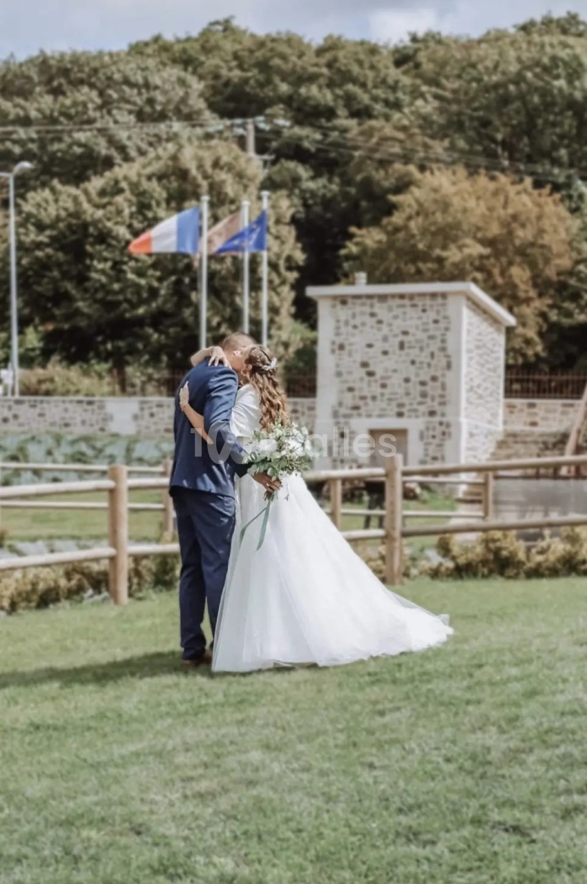 Un couple en tenue de mariage s'embrasse dans un jardin, avec des drapeaux et un bâtiment en pierre en arrière-plan.