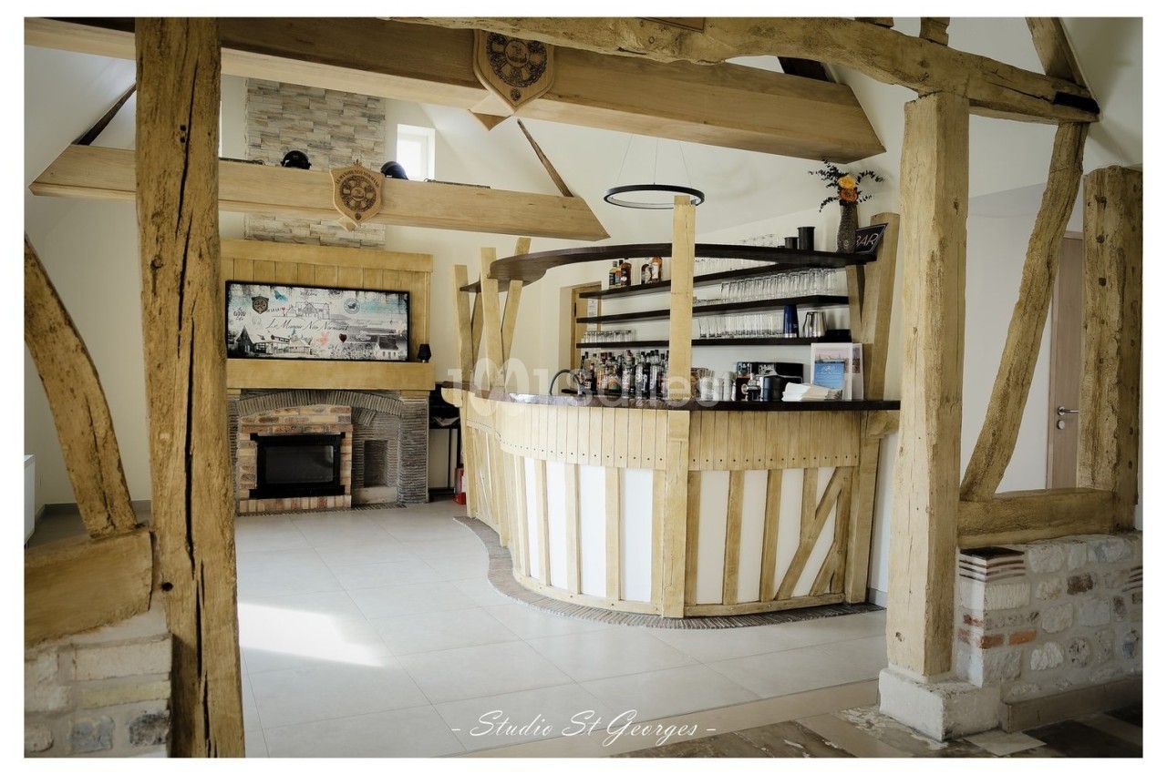 Comptoir en bois dans un espace lumineux avec poutres apparentes, cheminée et étagères garnies de bouteilles.