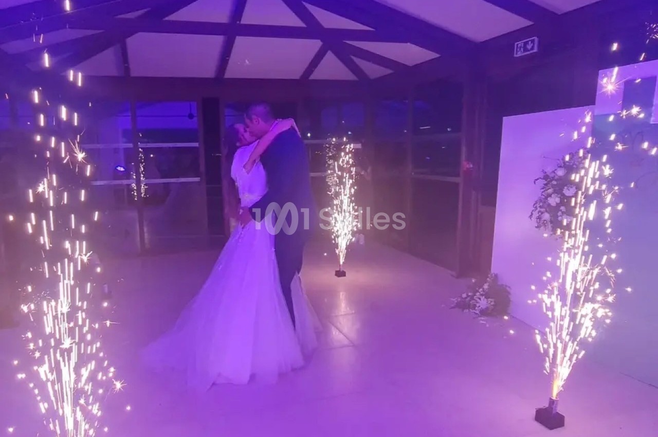 Un couple de mariés danse sous des étincelles lumineuses dans une salle éclairée par une lumière violette.