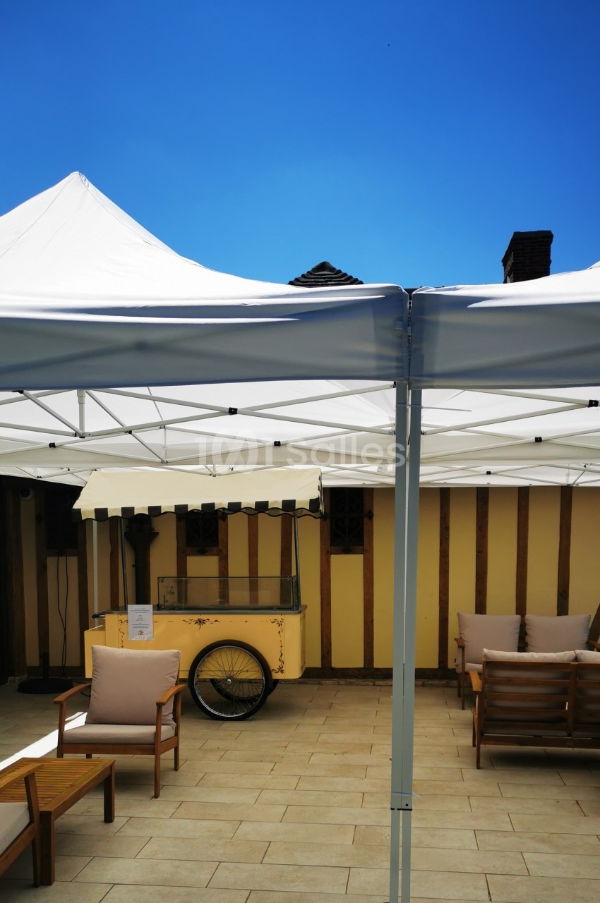 Tentes blanches installées sur une terrasse avec des fauteuils en bois et un chariot vintage en arrière-plan.