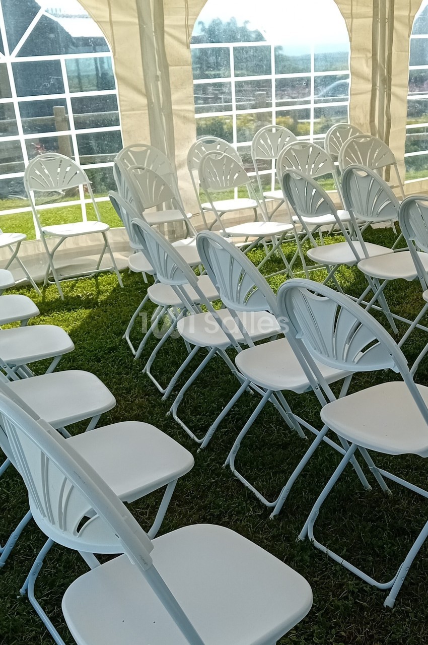 Chaises blanches pliantes alignées sous une tente, posées sur une pelouse verte par une journée ensoleillée.