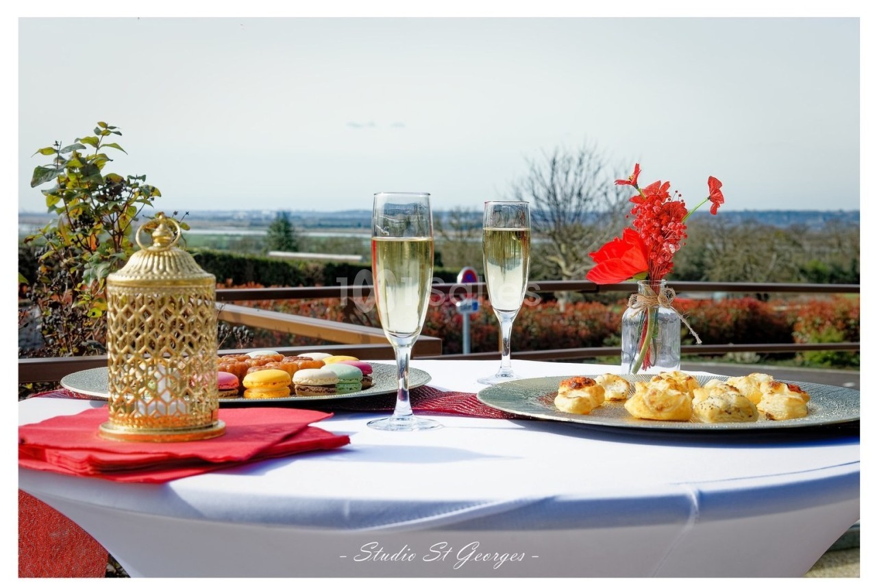 Table dressée en extérieur avec macarons, amuse-bouches, deux verres de champagne et une décoration florale rouge.