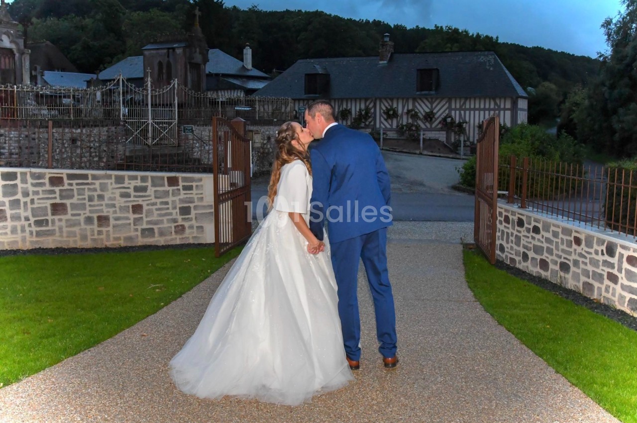 Un couple en tenue de mariage s'embrasse dans une allée pavée devant des bâtiments à colombages.