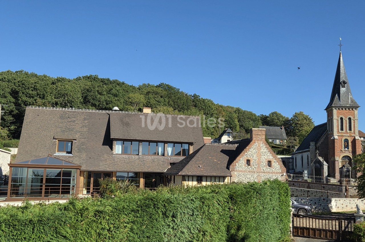 Manoir contemporain aux toitures d'ardoise avec extension vitrée, flanqué d'une église à clocher en briques rouges, en zone boisée.