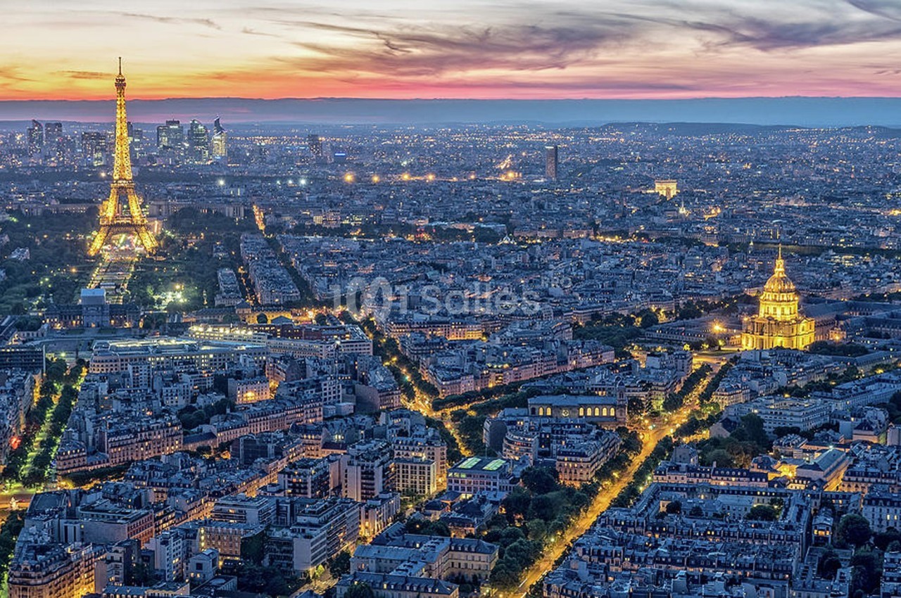 Vue aérienne de Paris au crépuscule, avec la tour Eiffel illuminée et les Invalides visibles au premier plan.