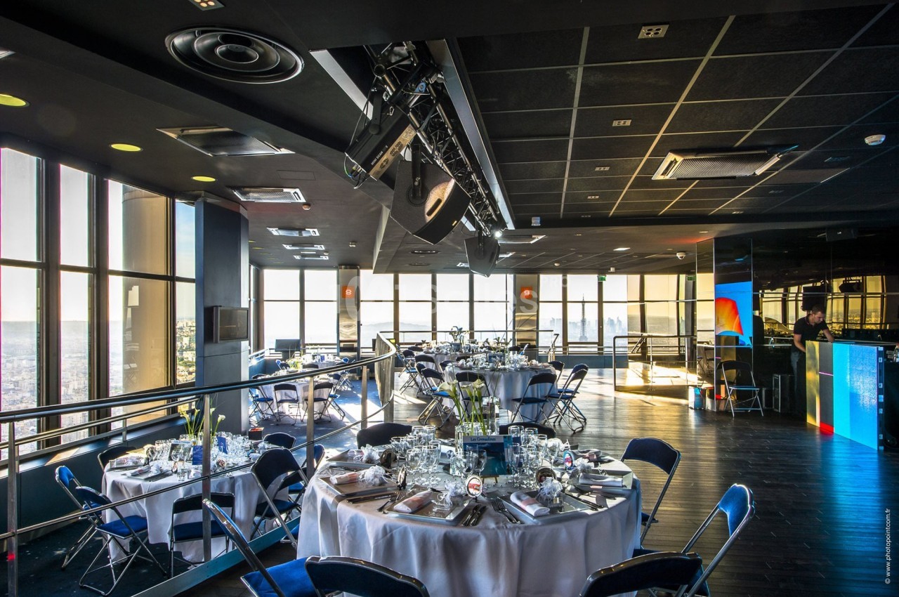 Salle de réception moderne avec tables dressées, grandes baies vitrées offrant une vue panoramique sur la ville.