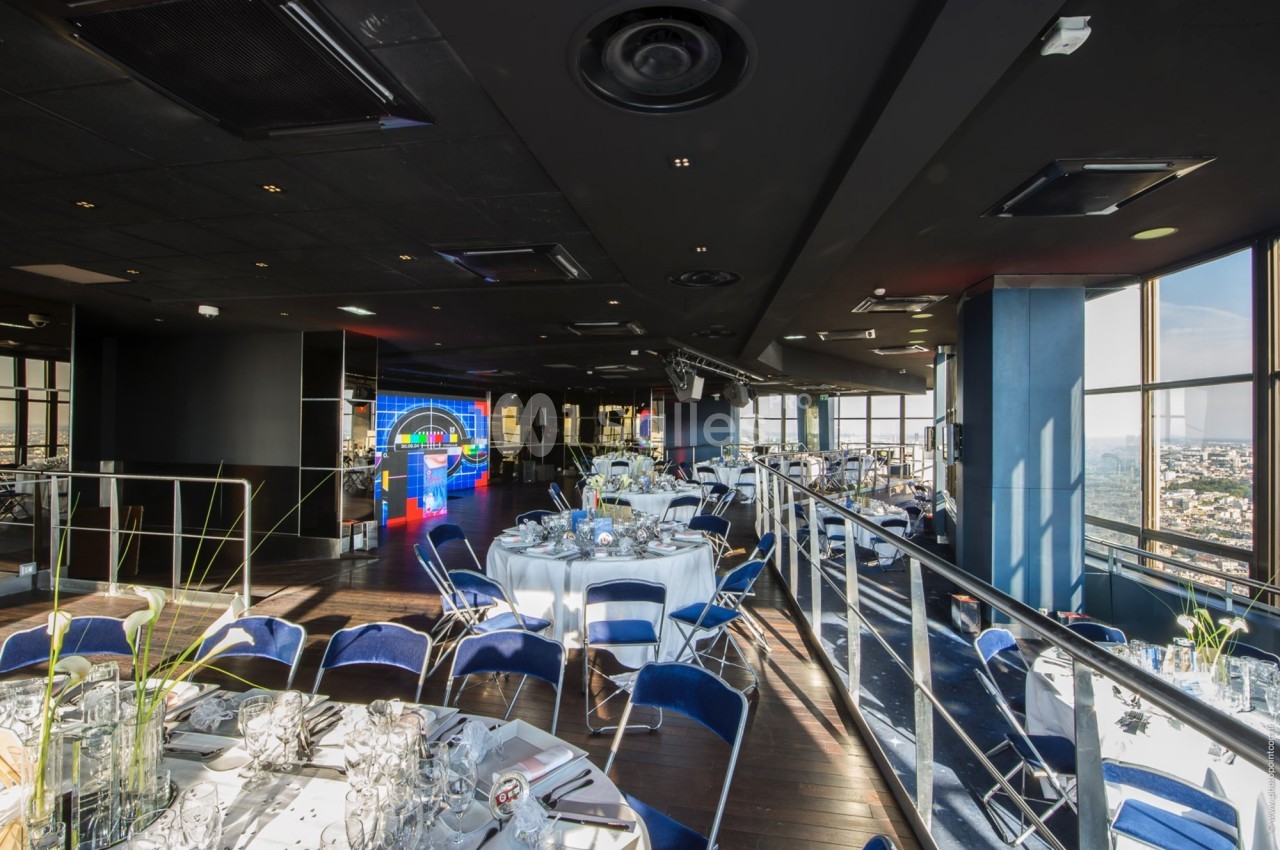 Salle de réception moderne avec tables rondes dressées, grandes baies vitrées et vue panoramique sur la ville.