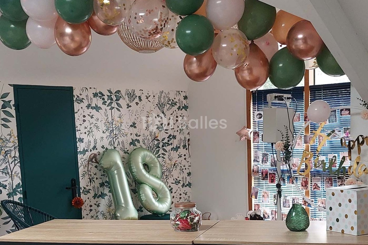 Décoration d'anniversaire avec ballons verts, blancs et dorés, chiffres ’18’ gonflés et guirlandes dans une pièce lumineuse.