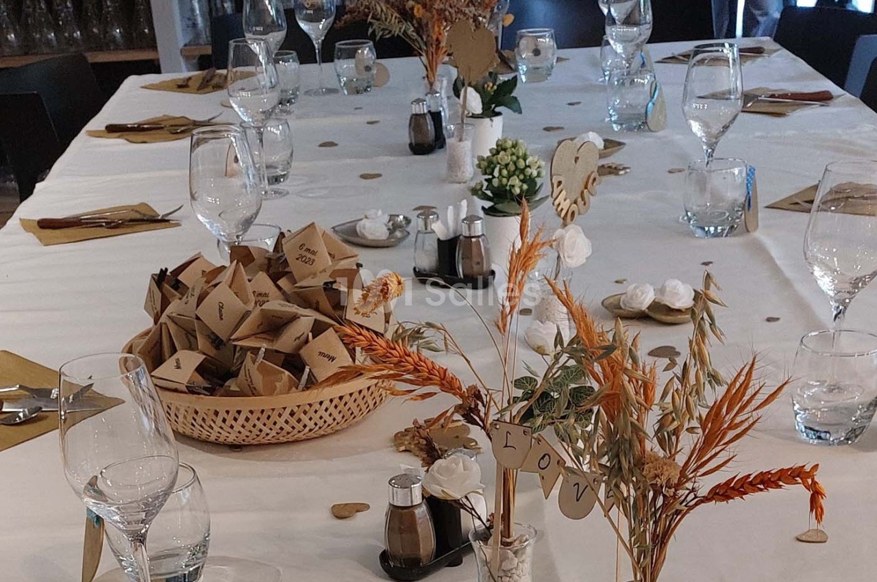 Table décorée pour un événement avec nappes blanches, verres, fleurs séchées et paniers contenant des petits sachets.