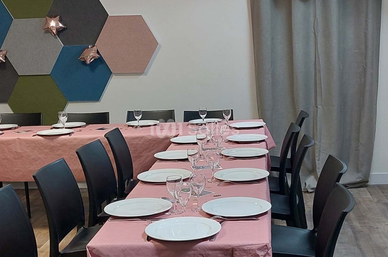 Tables dressées avec nappes roses, assiettes blanches et verres, dans une salle décorée de panneaux muraux colorés.