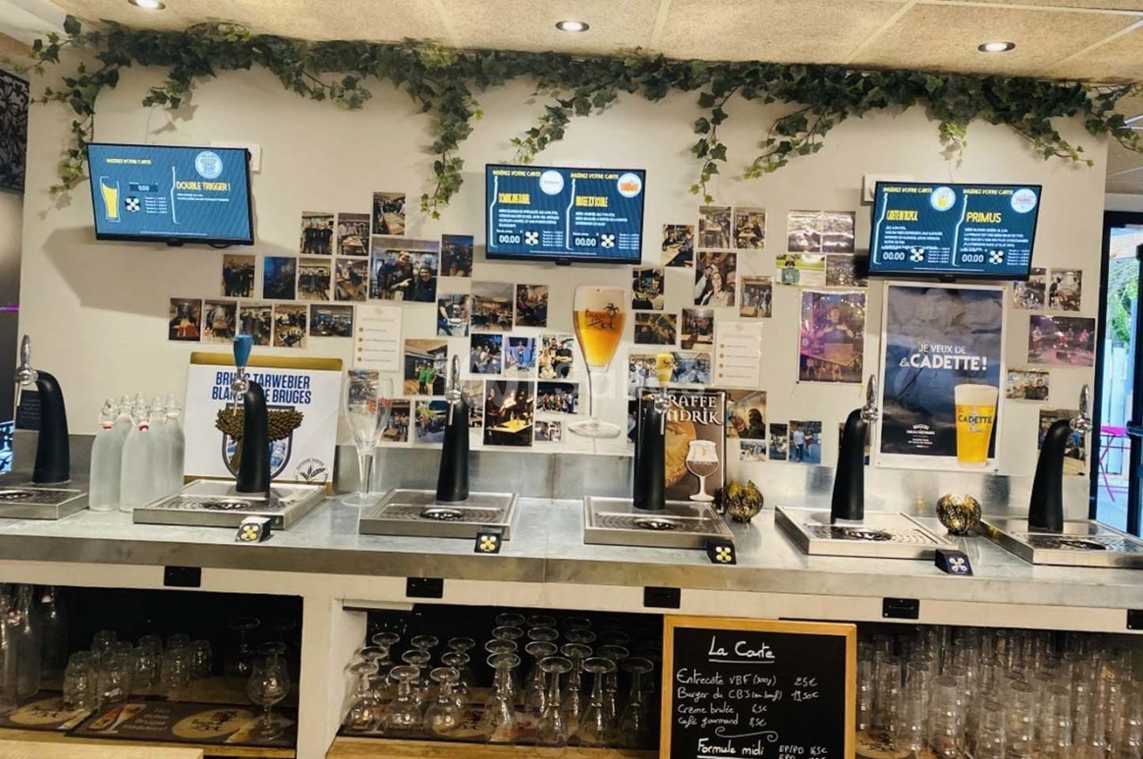 Comptoir de bar avec tireuses à bière, verres alignés, écrans d'affichage et décorations murales de photos.