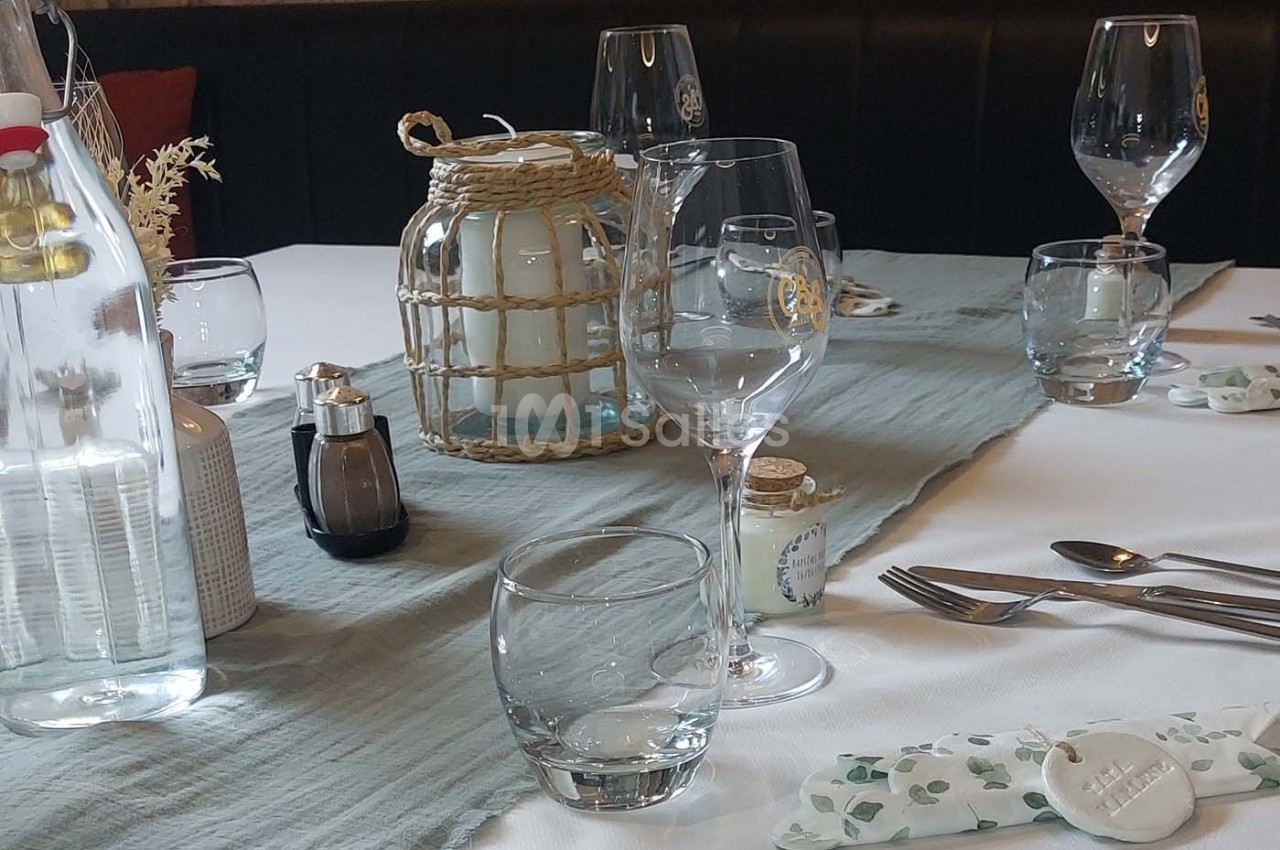 Table dressée avec nappe blanche, chemin de table bleu, verres, couverts, bougies et bouteille d'eau.