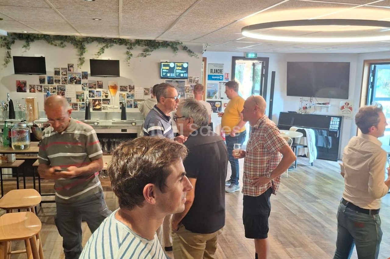 Des personnes discutent dans une salle conviviale avec des tables, des affiches au mur et un éclairage moderne.