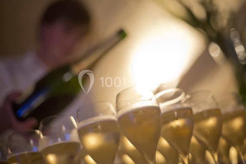 Personne servant du champagne dans des verres alignés, éclairés par une lumière douce en arrière-plan.