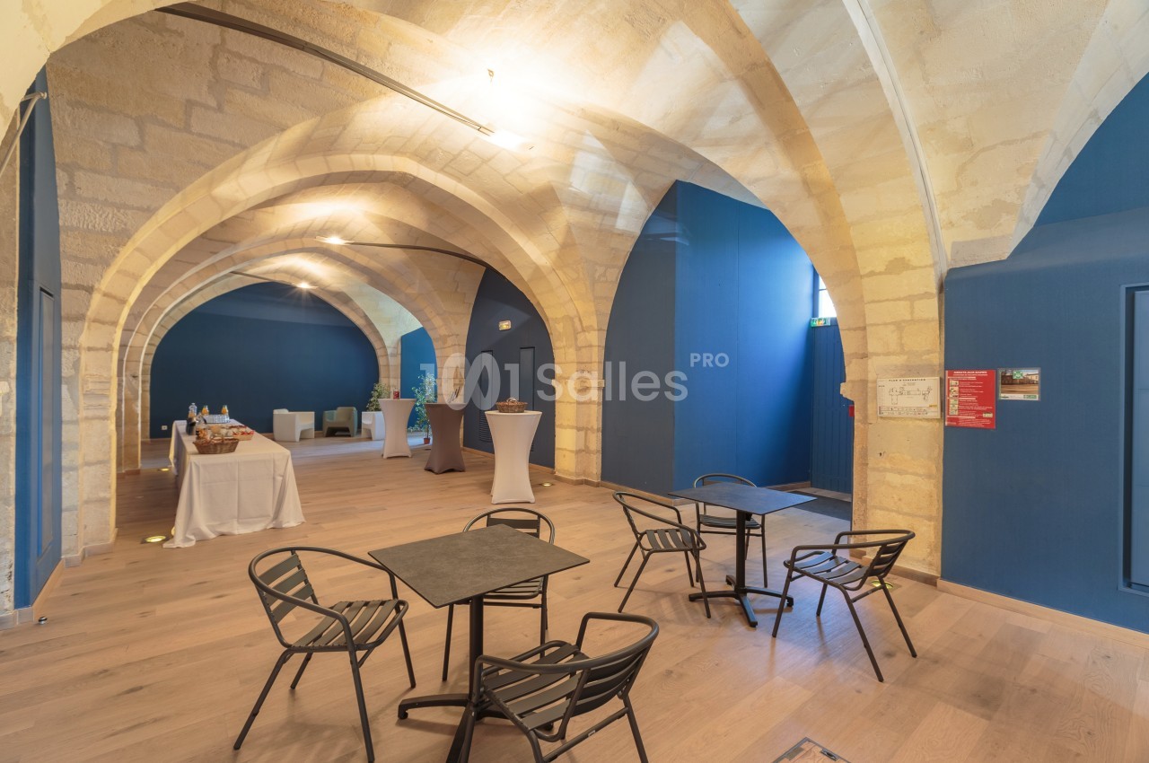 Salle voûtée avec murs en pierre, tables et chaises modernes, buffet en arrière-plan et éclairage chaleureux.