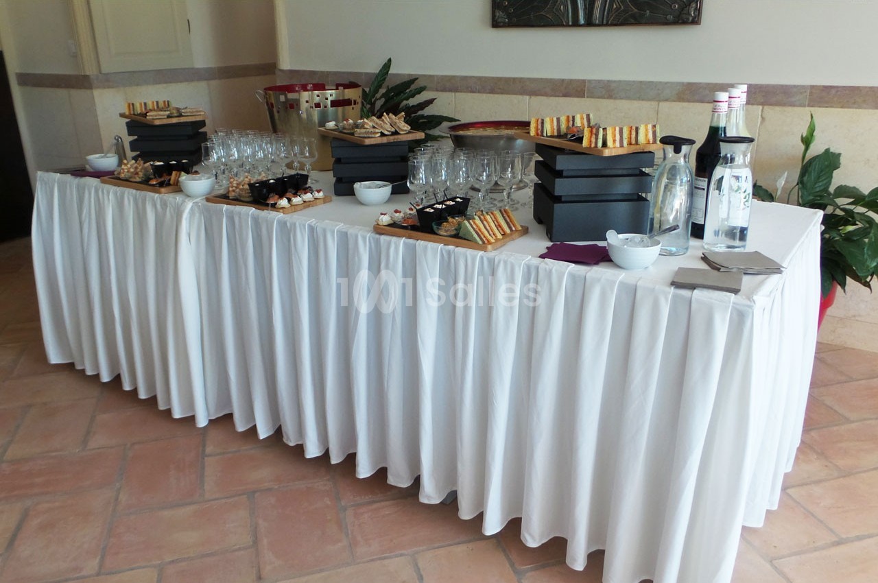 Table dressée avec nappage blanc, contenant des plateaux de bouchées apéritives, verres, bouteilles et seau à champagne.