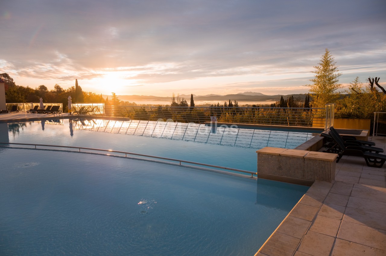 Piscine extérieure au lever du soleil, entourée de végétation et offrant une vue dégagée sur un paysage vallonné.