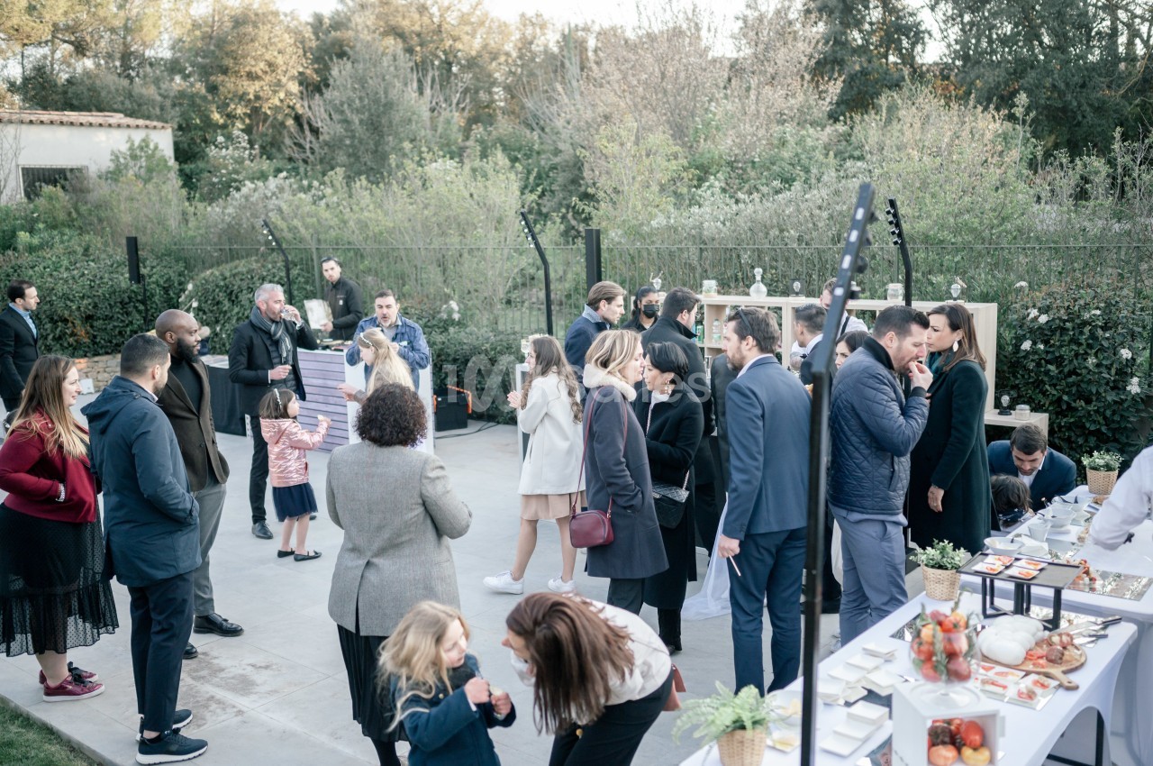 Groupe de personnes rassemblées en extérieur lors d'un événement, discutant près de tables avec des plats et boissons.
