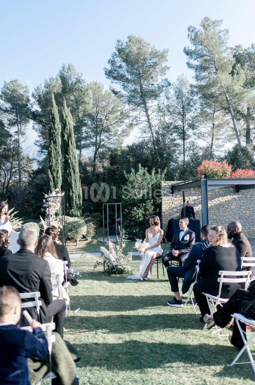 Cérémonie de mariage en extérieur avec des invités assis, un couple au centre et un décor naturel de verdure.