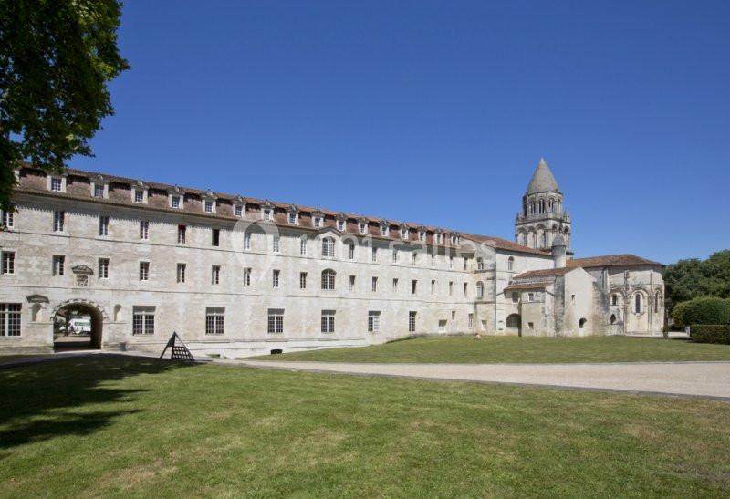 Bâtiment historique en pierre avec une tour, entouré d'une pelouse et d'arbres sous un ciel bleu dégagé.
