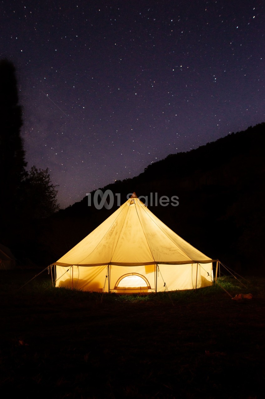 Tente éclairée sous un ciel étoilé dans un paysage nocturne calme.