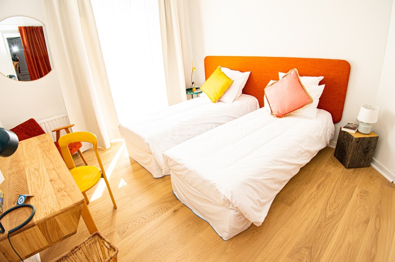 Deux lits simples avec tête de lit orange dans une chambre lumineuse, décorée avec des meubles en bois clair.