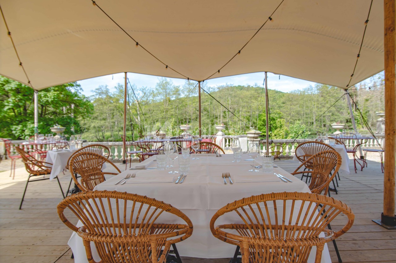 Terrasse extérieure avec tables dressées sous une tente, entourée de verdure et offrant une vue sur la nature.