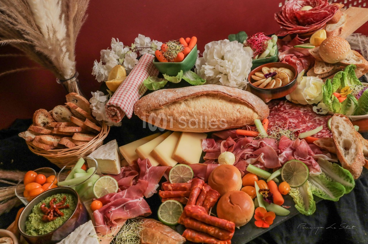 Plateau de charcuterie et fromages avec pain, légumes, fruits et sauces, disposés sur une table décorée.
