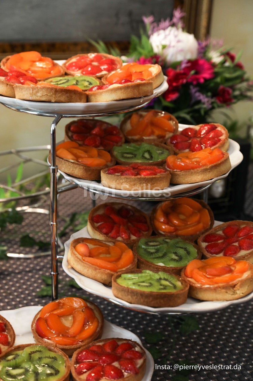 Plateaux de tartes aux fruits variés, garnies de kiwis, fraises et abricots, présentées sur un présentoir à étages.