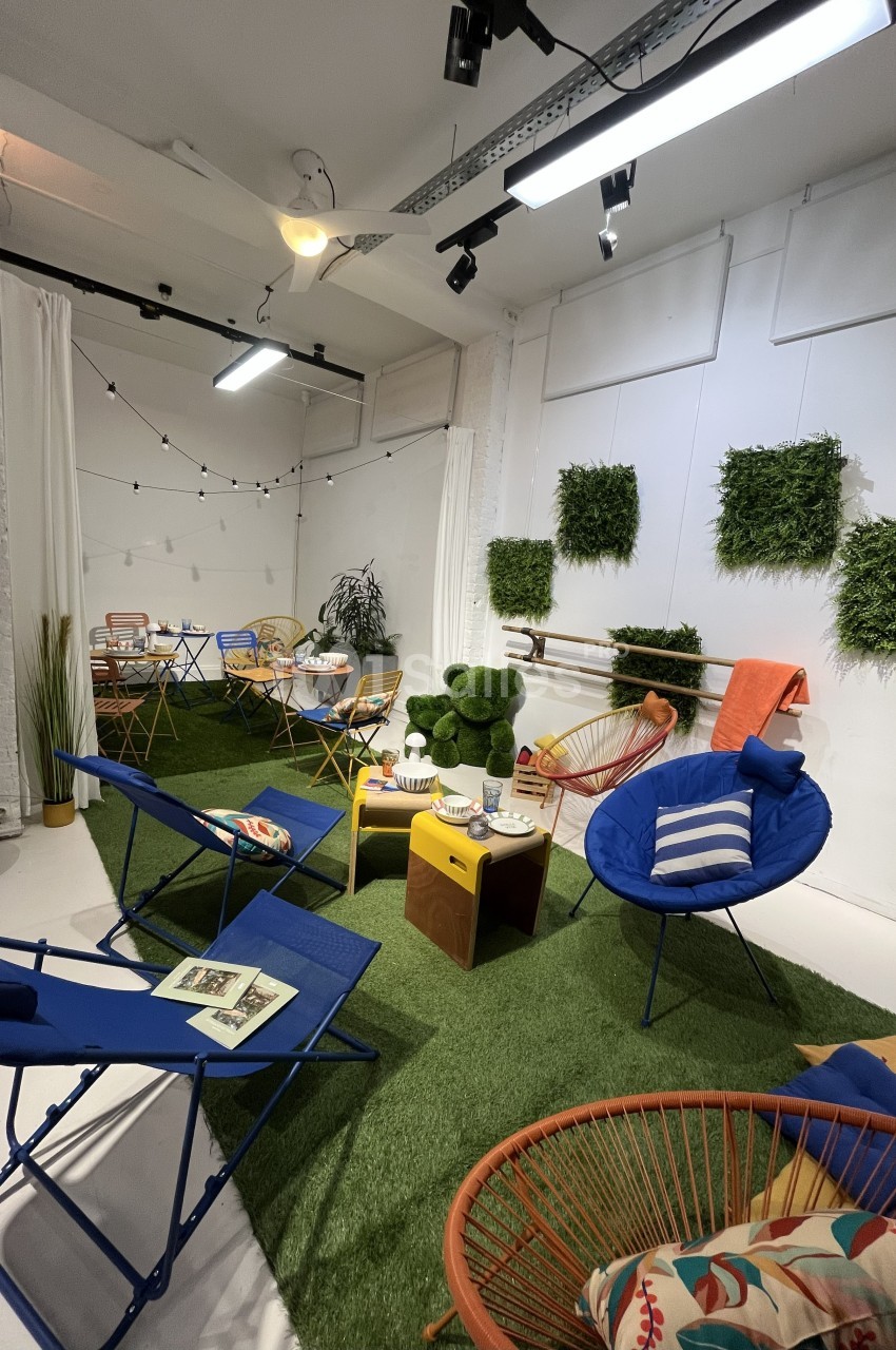 Espace intérieur aménagé avec des fauteuils colorés, des tables basses et un sol en gazon artificiel, décoré de plantes…