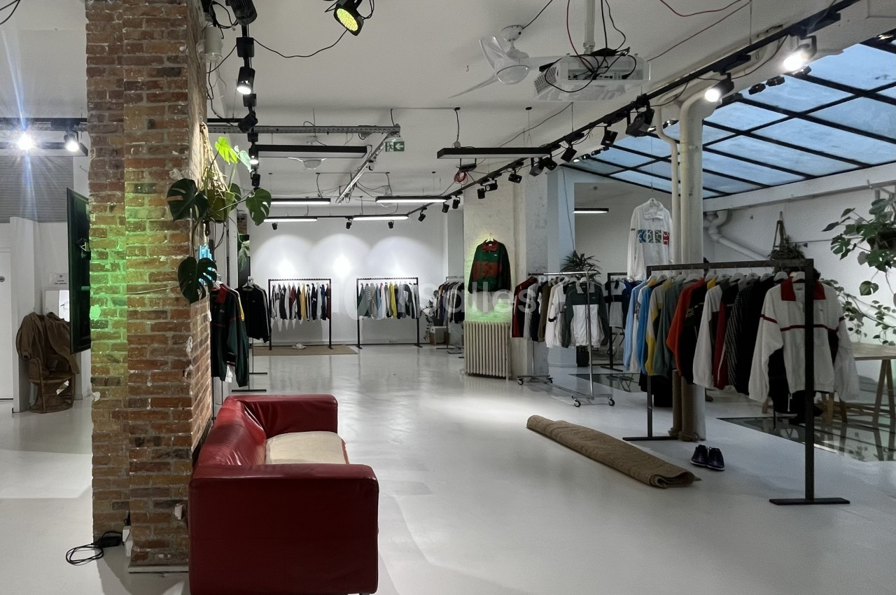Intérieur d'une boutique avec des vêtements suspendus sur des portants, un canapé rouge et un mur en briques apparentes.