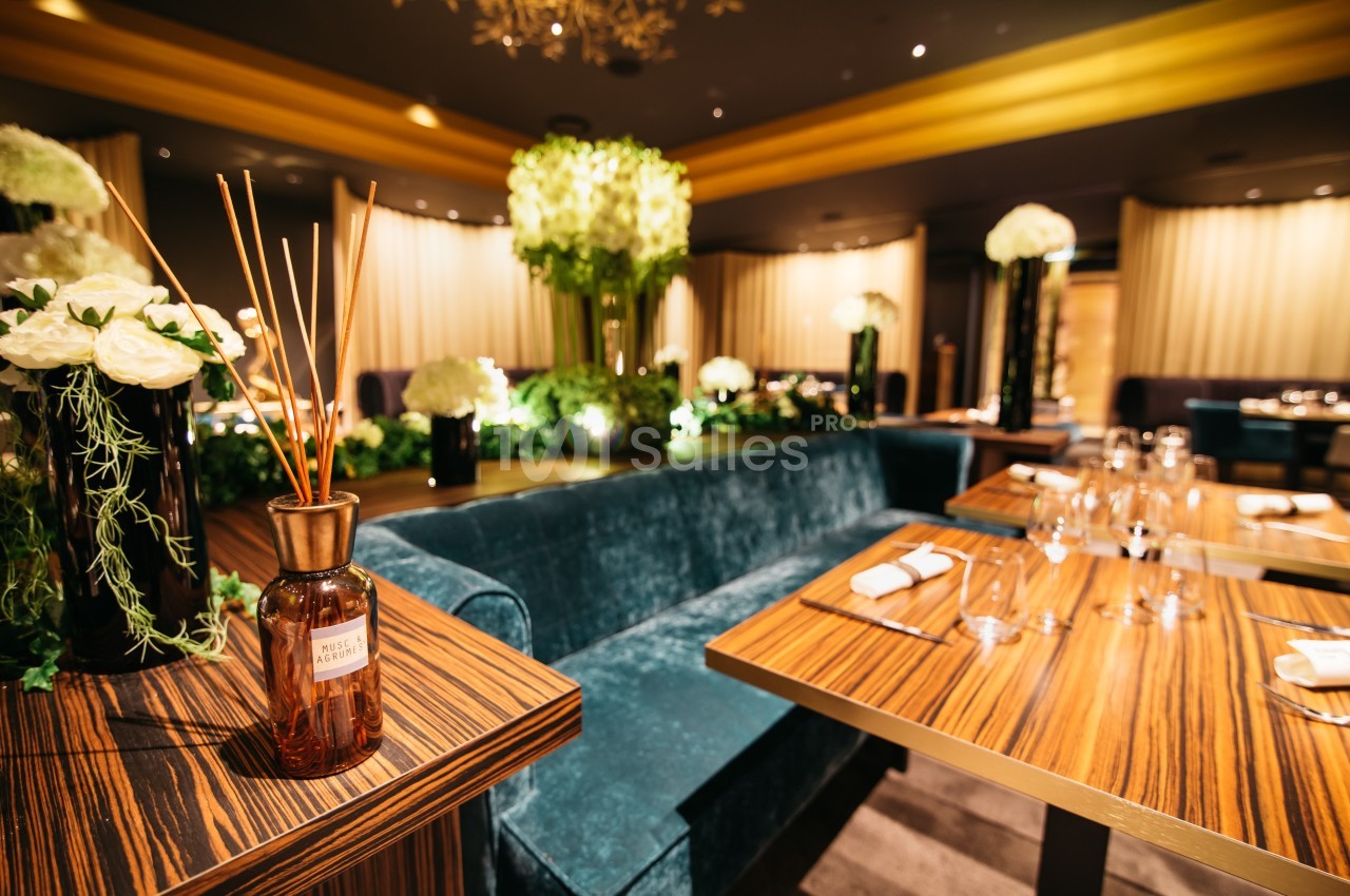 Salle de restaurant élégante avec tables en bois, banquettes en velours vert et décoration florale raffinée.