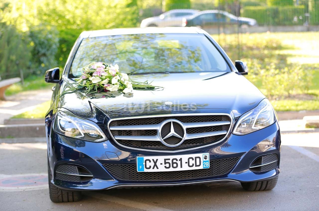 Voiture noire décorée de fleurs sur le capot, stationnée en extérieur par une journée ensoleillée.