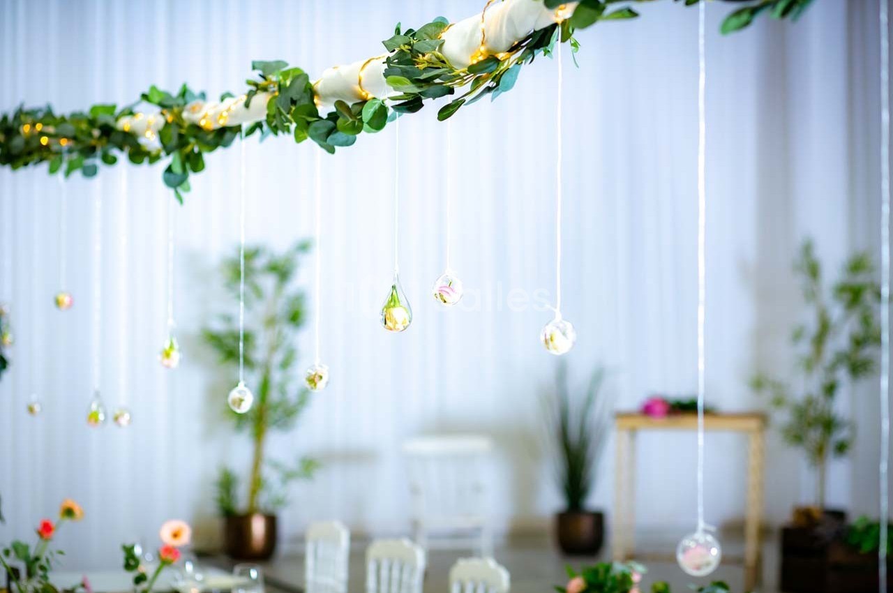 Guirlande végétale suspendue avec petites décorations en verre et fleurs, dans un espace lumineux et décoré.