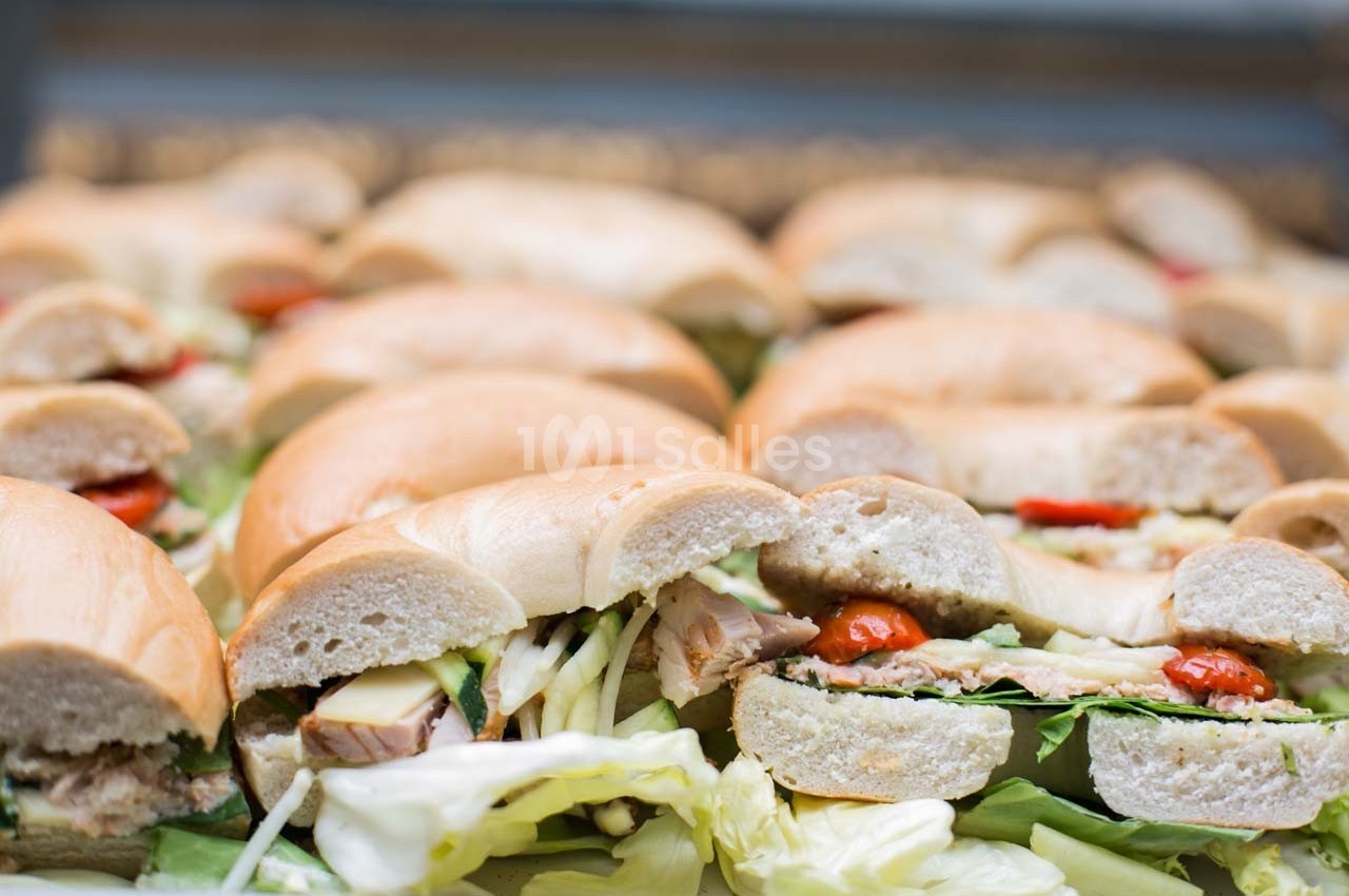 Bagels garnis de légumes, fromage et viande, disposés en rangées sur un plateau.