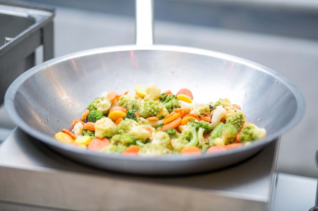Légumes variés, dont brocolis, carottes et chou-fleur, cuits dans un grand wok en métal.