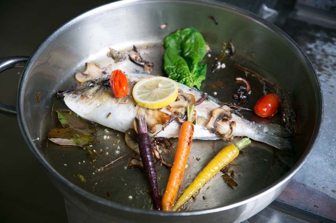 Poisson entier cuit dans une poêle avec légumes colorés, champignons, tomate cerise et tranche de citron.