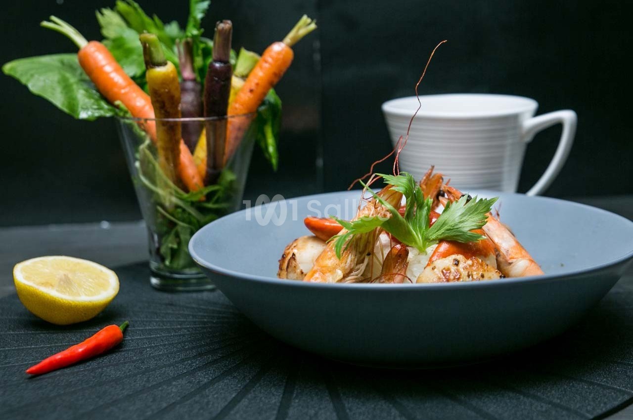 Assiette de fruits de mer avec crevettes et herbes fraîches, accompagnée de légumes colorés et d'une tasse blanche.